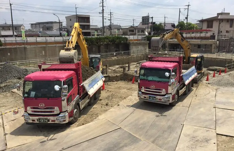 工事現場で土砂を積み込む2台のダンプカーとバックホウ